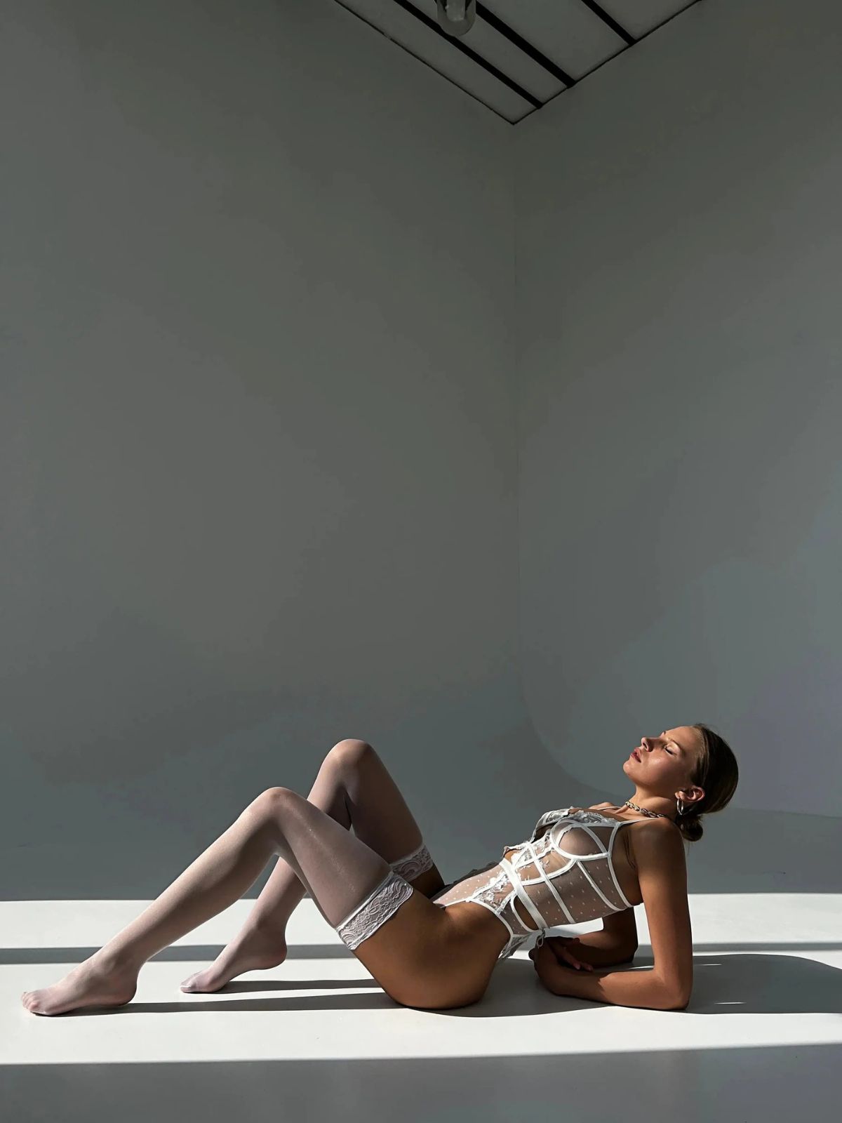 Allure Sheer Bodysuit - White reclining pose with soft lace and polka-dot fabric for an ethereal and romantic look.