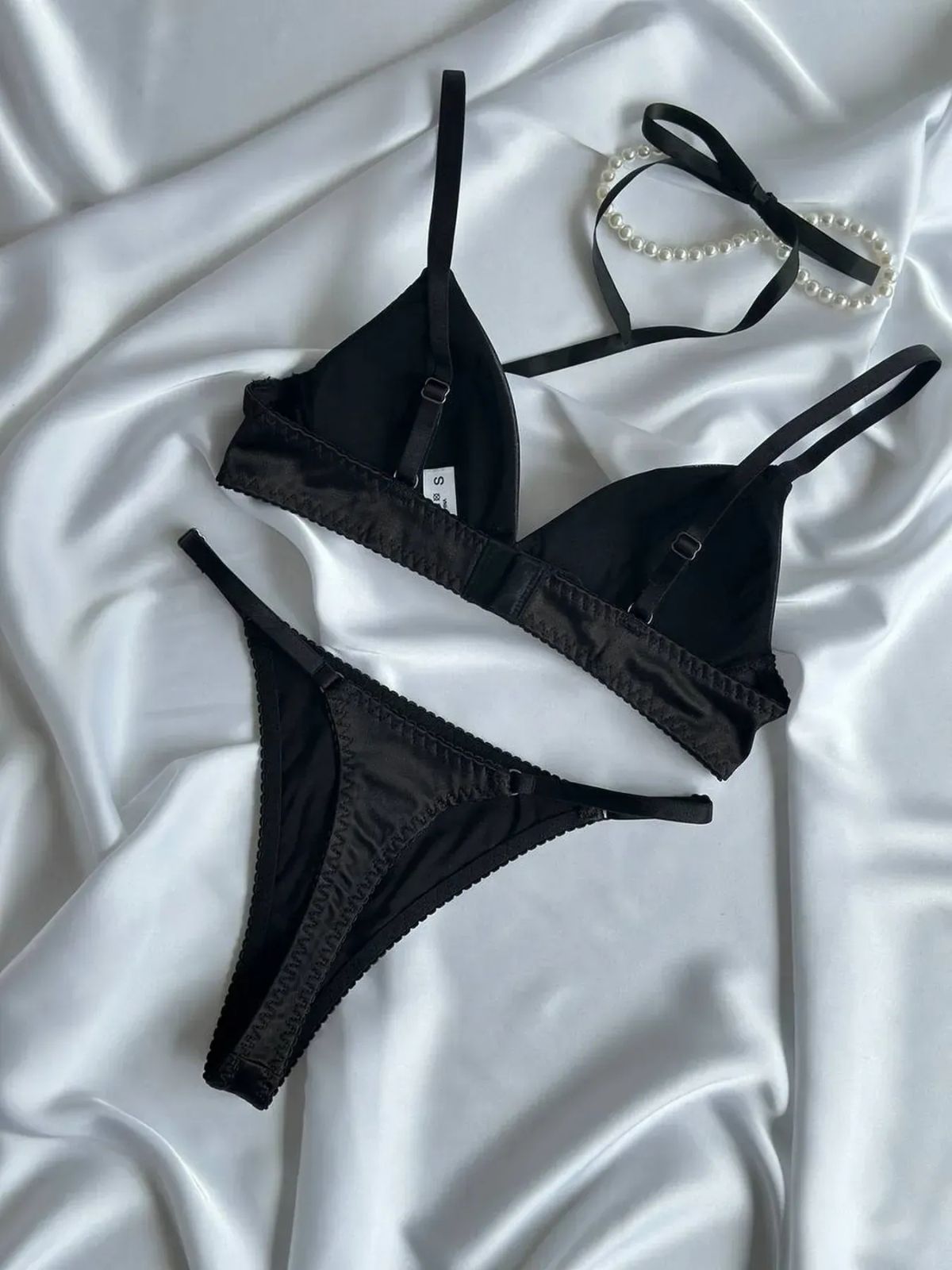 black push up bra set flat lay on white satin, bra and thong with pearl accessory