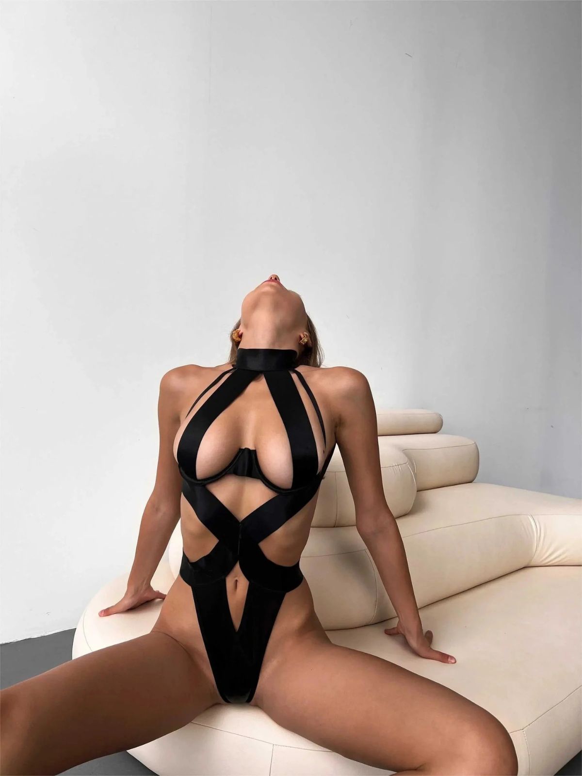 Elysian Open Back Bodysuit-Black in a bold lounging position, highlighting its sleek and daring design.