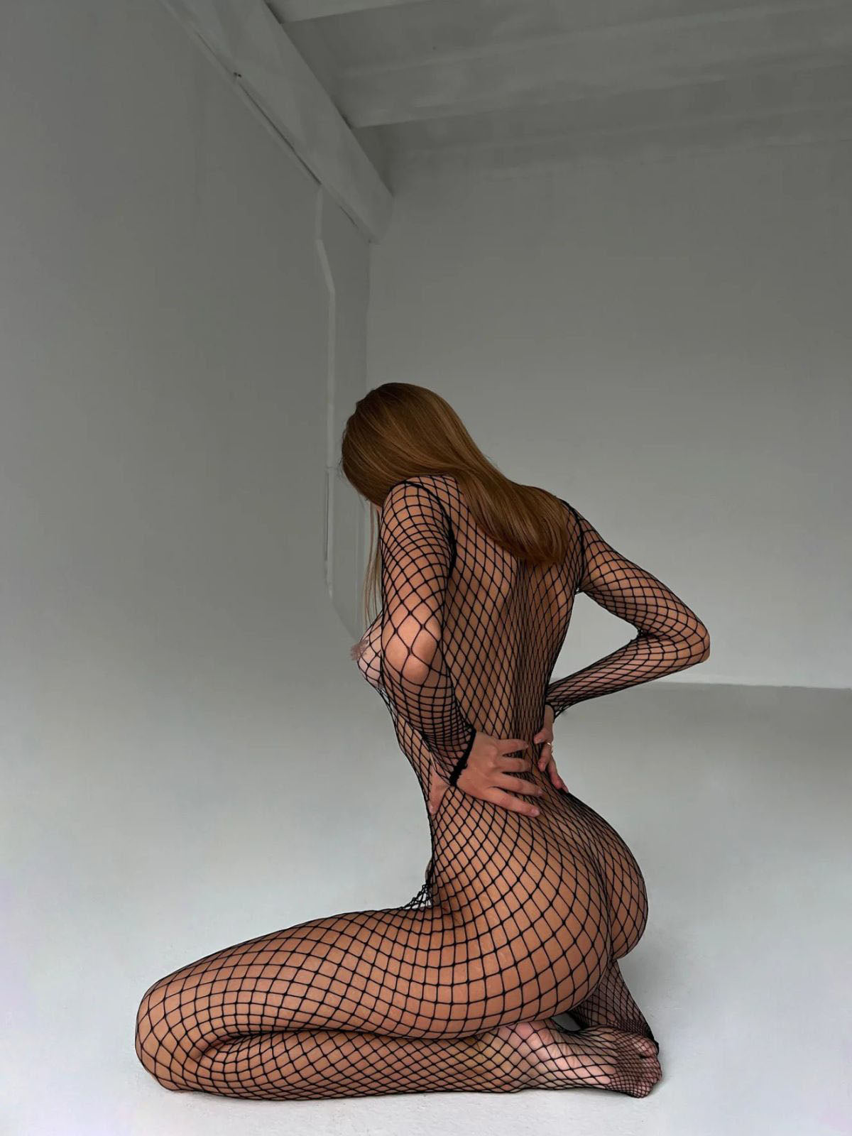 fishnet bodystocking black long sleeve catsuit, back view kneeling with wide mesh and sleek fit