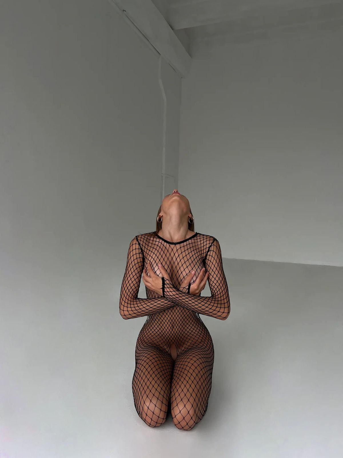 fishnet bodystocking black long sleeve catsuit, front kneeling pose in studio with full-body net