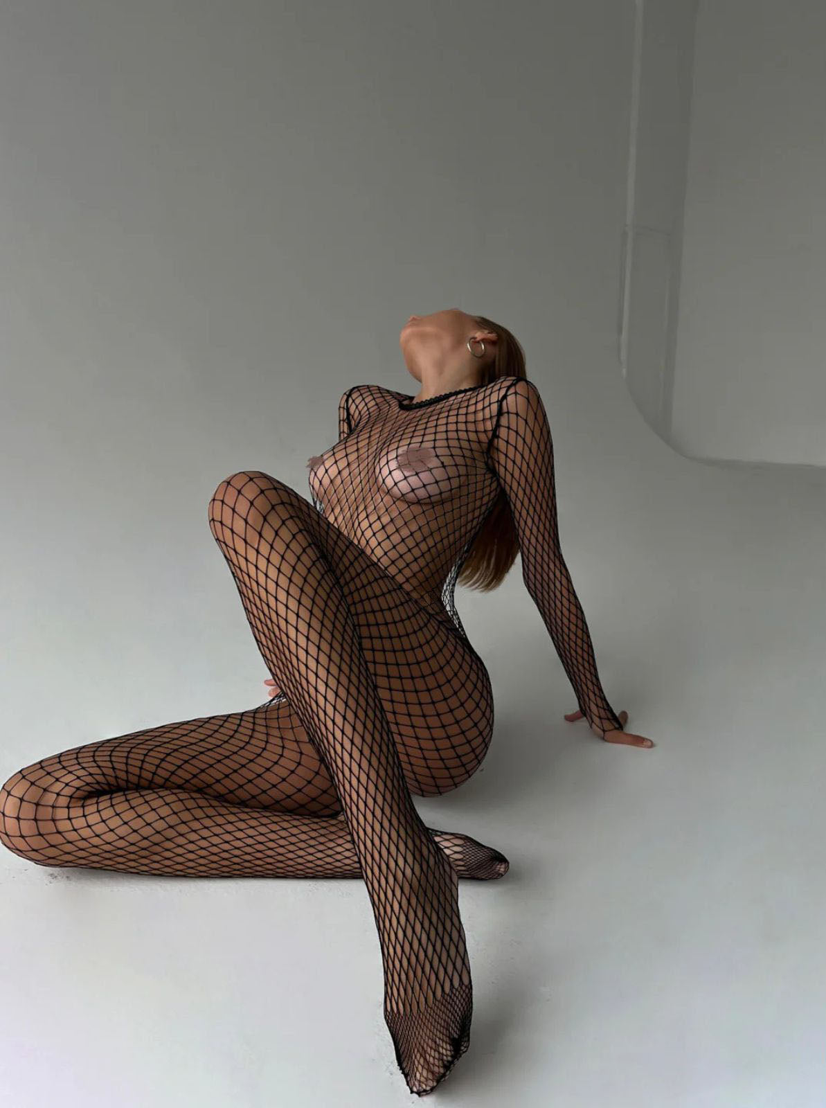 fishnet bodystocking black long sleeve catsuit, seated side profile in studio with wide net mesh