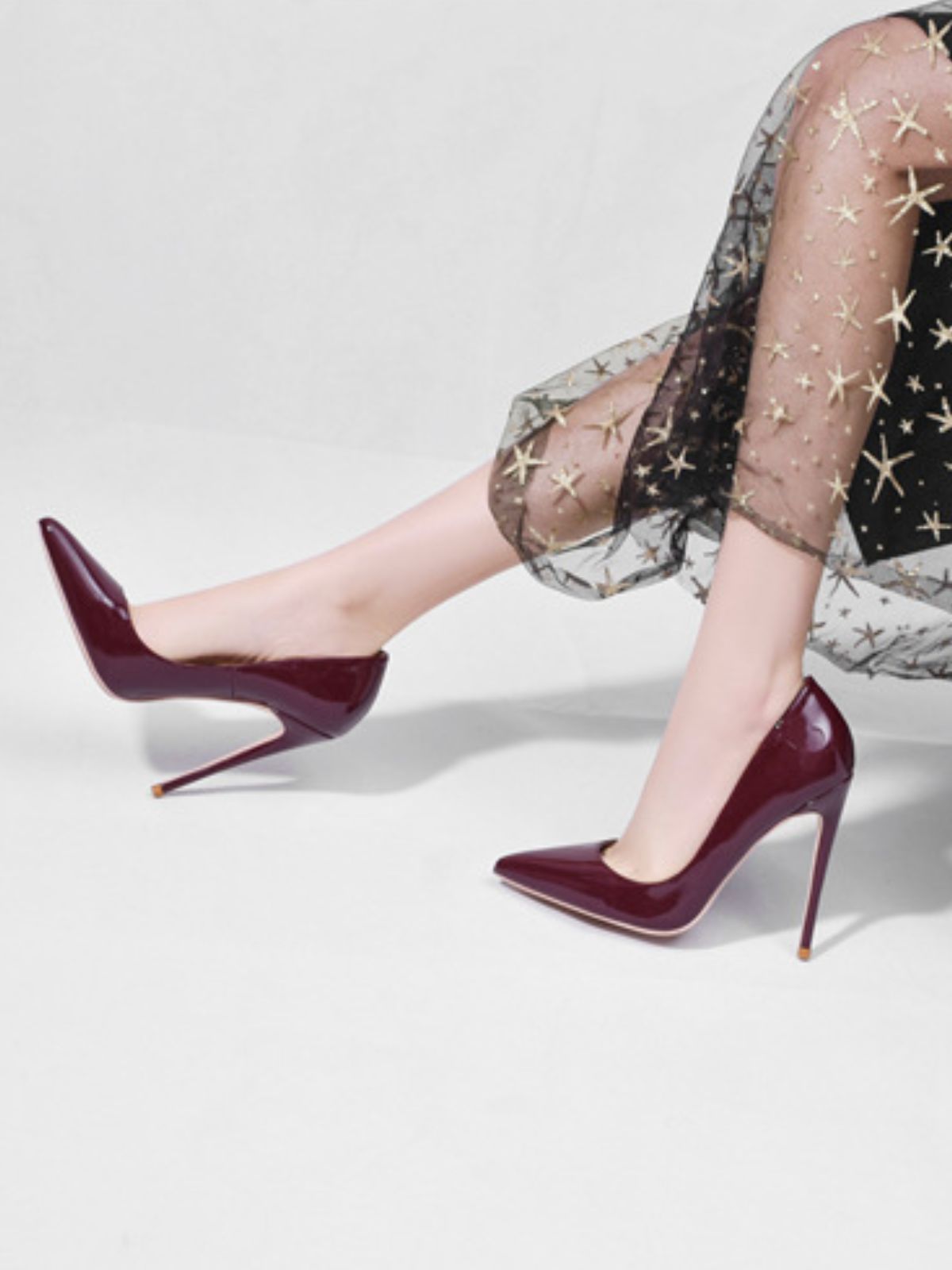 Glamour Stilettos Heels – Wide Fit deep burgundy patent stilettos on model sitting in star-print skirt