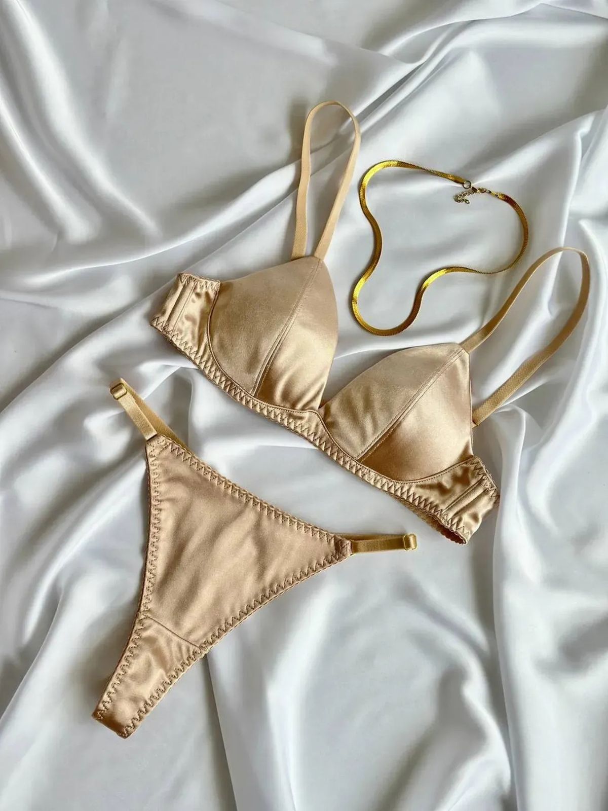 nude push up bra and thong set flat lay on white satin, nude lingerie with gold necklace