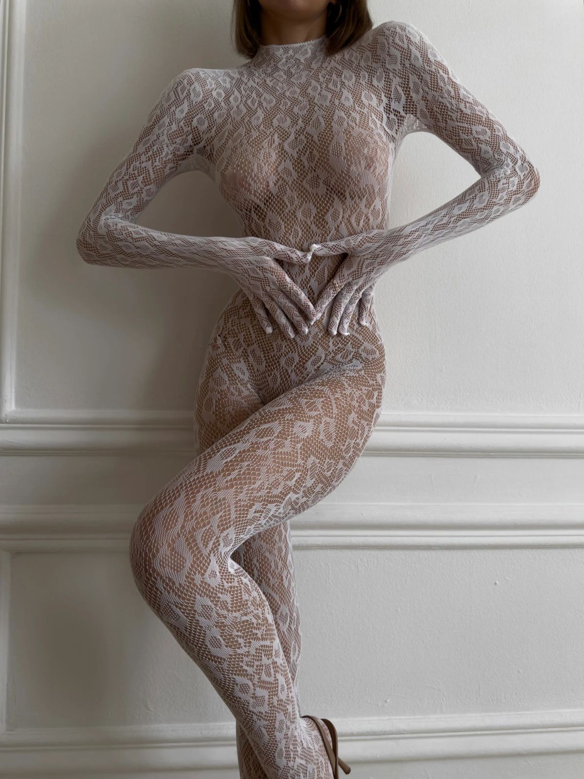 Seductive Sheer Full Bodysuit in white, with a chic pose and crossed legs, showcasing elegance.