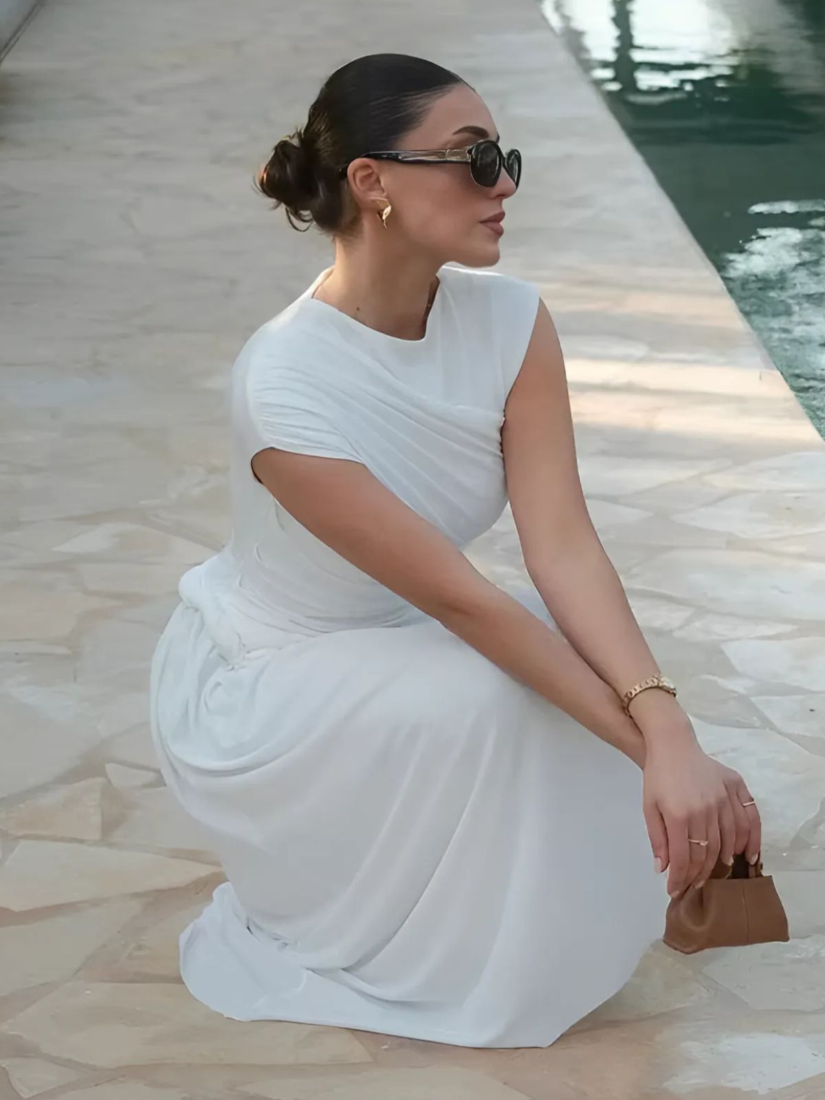 White elegant bodycon maxi dress styled while seated, highlighting graceful pleats and sleek lines.